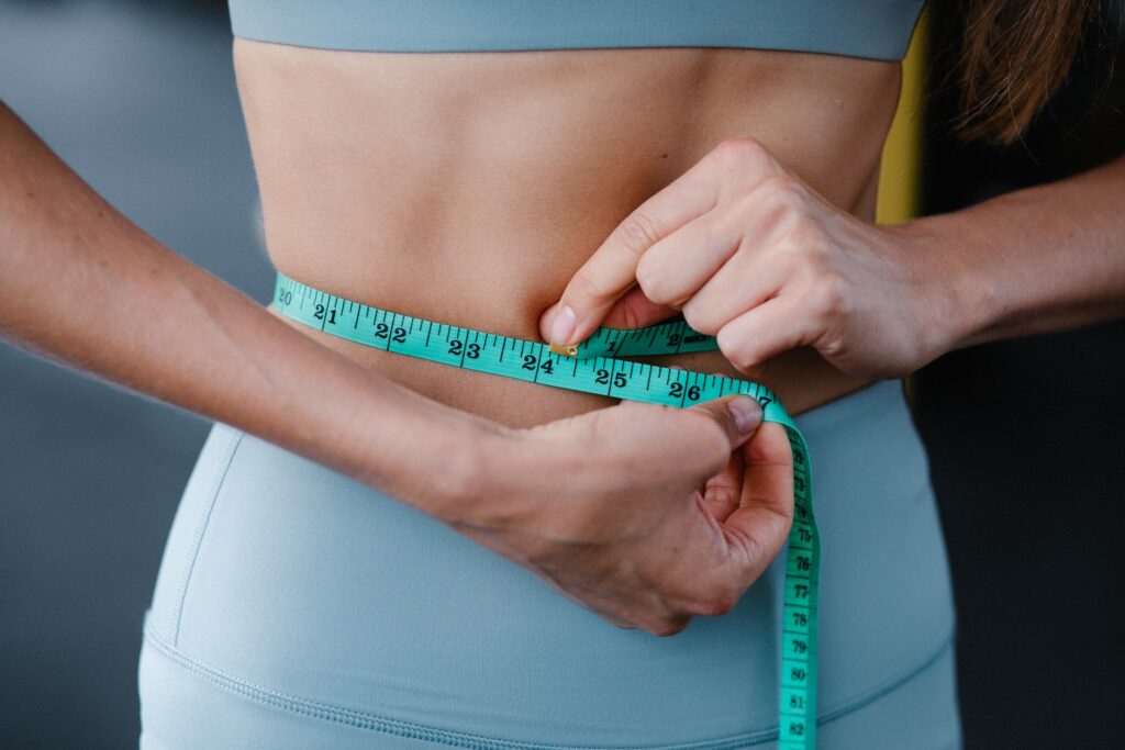 Woman in athletic wear measuring her waist with a measuring tape.